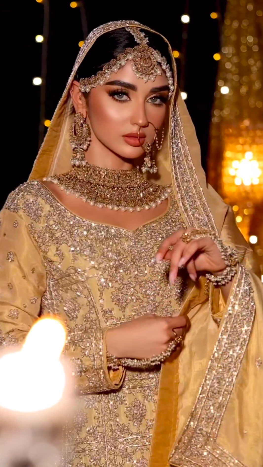 Woman in traditional embroidered outfit with jewelry against a warm, blurred background